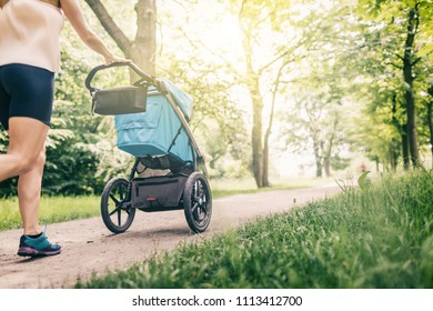 Running woman with baby stroller enjoying summer day in park. Jogging or power walking supermom, active family with baby jogger.