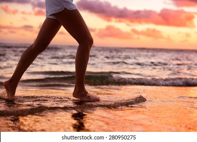 Running Woman Jogging Barefoot In Water At Beach Sunset. Close Up Of Female Feet Of Runner Splashing In The Edge Of Water. Girl Training Alone.