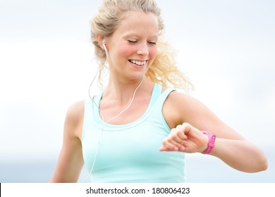 Running Woman Looking At Heart Rate Monitor Watch Outside Jogging On Beach. Female Fitness Runner Girl Jogger Training Outdoors Listening To Music In Earphones. Beautiful Young Blonde Woman In Her 20s