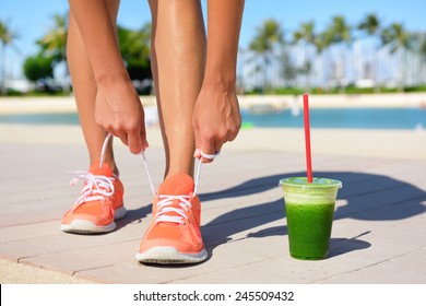 Running woman runner with green vegetable smoothie.  Fitness and healthy lifestyle concept with female model tying running shoe laces.