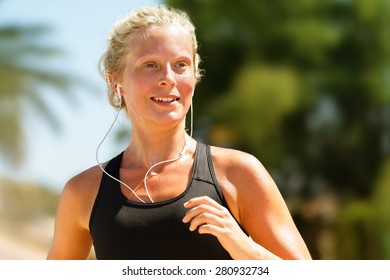 Running Woman Sweating Workout With Earphones. Female Runner Listening To Music In Earbuds. Girl Athlete Jogging City With Palm Trees. Healthy Lifestyle Concept With Young Blonde Fitness Model.