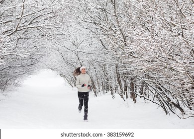 Running In The Woods In Winter. Beautiful Young Woman Running Jogging In The Winter Forest. Trees In The Snow. Weather Snow Cloud. Fitness On The Street In The Winter.