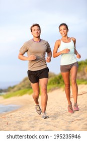 Running Young Mixed Race Couple Jogging Outside On Beach Happy Smiling In Summer Sunset. Caucasian Handsome Male Model And Asian Fitness Female Model.