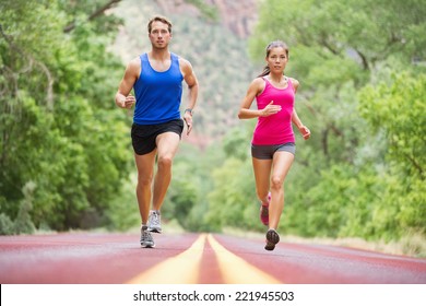 Running Young People - Two Runners Jogging On Road In Nature Training For Marathon Run. Multicultural Couple - Asian Mixed Race Beautiful Model Woman And Caucasian Male Fitness Model Exercising