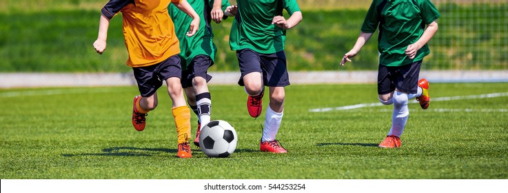 Running Youth Football Players. Kids Playing Football Soccer Game On Sports Field. Boys Play Soccer Match On Green Grass. Youth Soccer Tournament Teams Competition. 