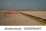 A runway holding point on a deserted airfield, marked by yellow lines and a red "runway direction" marking