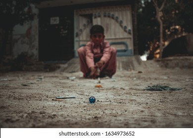 Rural Areas/Sindh/pakistan, February 1 2020, A Little Poor Kid Playing With Marbles Toys,trying To Hit A Marble Ball With Another Marbel Ball.