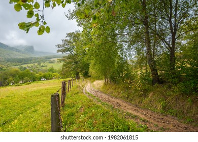 rural dirt road to village. autumnal countryside of carpathian mountains. rainy weather. fence along the meadow. gray heavy clouds above the valley