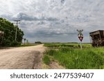 Rural farm road in Cloud County, Kansas. Leading over railroad tracks; railroad car visible. Trees, green fields beyond. Cloudy sky overhead.
