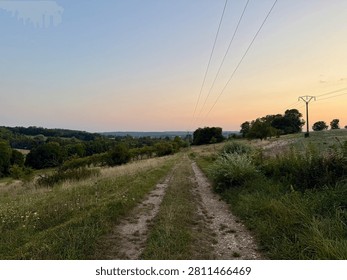 Rural footpath through meadows and orchards above a village at dusk in the Vosges countryside, Lorraine, France