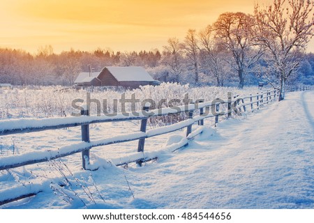 Rural house with a fence in winter. Village after snowfall