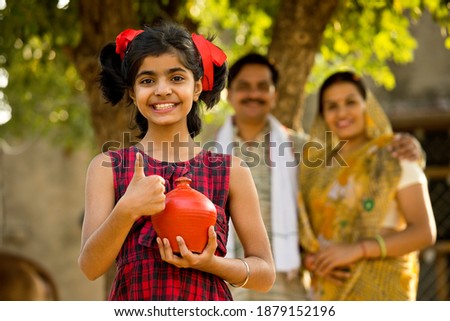 Rural Indian family with surprised daughter holding piggy bank