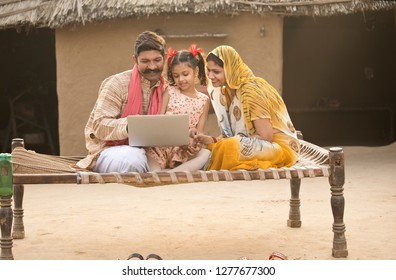 Rural Indian Family Using Laptop On Traditional Bed At Village