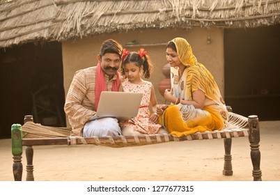 Rural Indian Family Using Laptop On Traditional Bed At Village