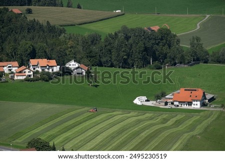 Similar – A tractor turns mown hay in a field in a small community