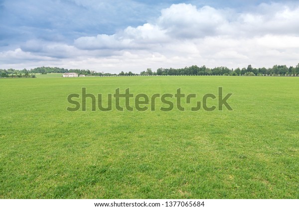 Rural landscape. The flat well-groomed field\
of a short-haired grass, a country house in the distance at the\
hill. The beautiful cloudy sky in sunny\
day