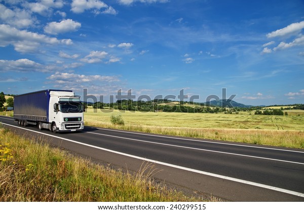 Rural landscape with road you are driving\
a white truck, in the background of a green cornfield and wooded\
mountains, white clouds in the blue\
sky