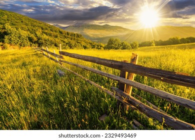 rural landscape at sunset. wooden fence near the grassy meadow and trees on the hillside. beautiful countryside scenery in evening light - Powered by Shutterstock