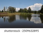 Rural landscape view of a small pond located in a natural area called "Plateau des 1000 etangs" in Haute-Saône department in France. Picture taken 29 August 2024. Green vegetation and trees visible. 