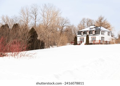 Rural patrimonial white house with metal sheet mansard roof seen in winter surrounded by bare trees and snowy land, Neuville, Quebec, Canada - Powered by Shutterstock