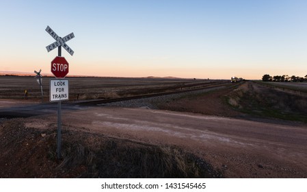 A rural railway crossing at sunset in South Australia, a train approaches from the South. 