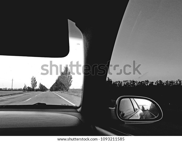 Rural road from car window. Sunset in the mirror.\
Black white photo