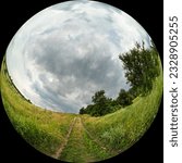 Rural road to the hill with trees and grass. Cloudy day with clouds in the sky. Wide angle fisheye photo in circular format