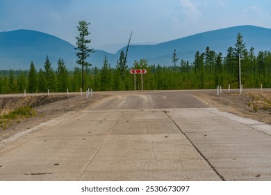 A rural road intersection surrounded by a forest of trees with distant mountains in the background under a cloudy sky. The scene is calm and remote, with no people in sight - Powered by Shutterstock