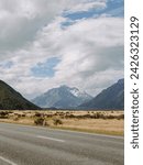 Rural road side view of beautiful destination snow covered mountain peaks and dry grass farmland in New Zealand South Island landscape