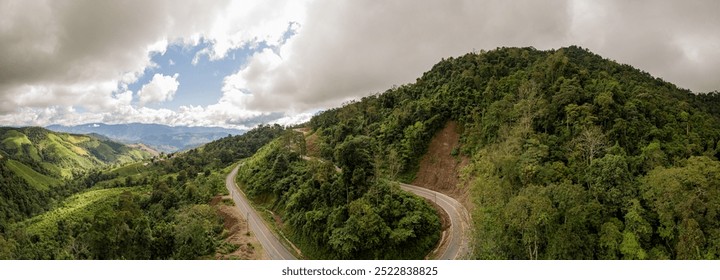 A rural road winds through a serene mountain vista, bordered by lush green forest under a blue sky at dawn in Doi Phuka National Park, Nan Province, Thailand - Powered by Shutterstock