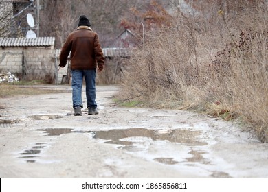 Rural scene, man in jeans and dirty galoshes walks on a rural street with puddles. Rainy weather in village