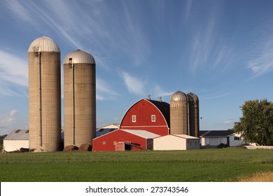 Rural scene showing a modern family farm with a bright red barn surrounded by silos.  Dramatic blue sky with wispy clouds.  The sky also provides text space if needed.