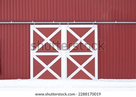 Rural scene of sliding doors with a white crisscross pattern that are closed shut on a barn with red metal siding.