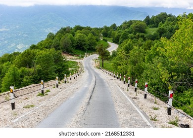 Rural Tarmac Winding Downhill Road Covered With Loose Stones And Gravel From Khvamli Mountain Peak Down To Tskhenistsqali River Valley With Lush Green Trees Around And Mountain Landscape.