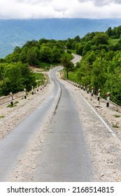 Rural Tarmac Winding Downhill Road Covered With Loose Stones And Gravel From Khvamli Mountain Peak Down To Tskhenistsqali River Valley With Lush Green Trees Around And Mountain Landscape.