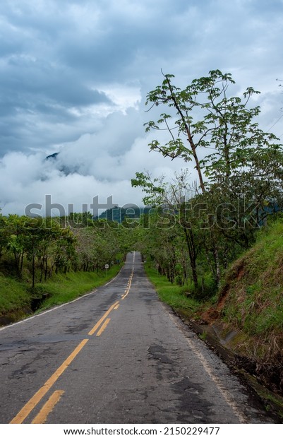Rural two lane highway with mist shrouded\
mountains in the background.\
Colombia