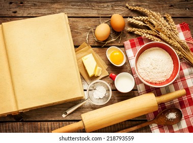 Rural Vintage Wooden Kitchen Table With Blank Cook Book, Baking Cake Or Dough Ingredients (eggs, Flour, Milk, Butter, Sugar) And Cooking Utensils Around. Background With Free Recipe Text Space.