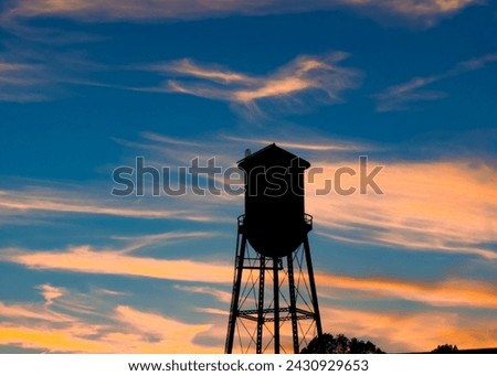 Rural water tower tank against a beautiful sunset on an autumn day.