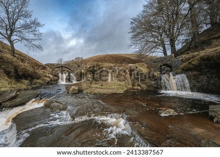 A rural winter landscape scene of the waterfall and packhorse stone bridge at Three Shires Head in the Peak District National Park.