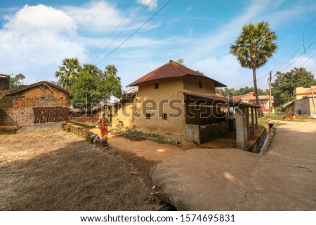 Rural woman walking along an unpaved village road with view of mud hut at a tribal Indian village at Bolpur, West Bengal