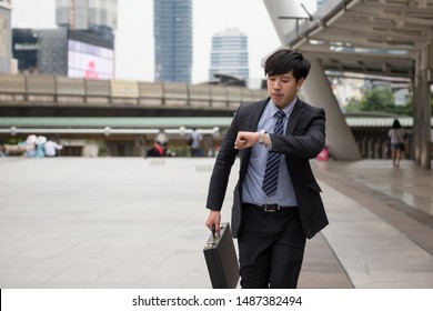 Rush Asian Chinese Businessman Running And Looking At Watch To Check Time On City Walk. Young Man Late For Train Transportation, Work, Meeting. Office Life And Business Competition.