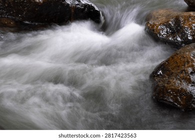 Rushing River Currents The dynamic flow of a powerful river cascades over smooth, weathered rocks, creating a mesmerizing display of whitewater and motion.