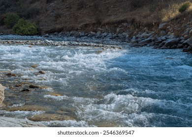 A rushing stream of blue water in a mountain river. Steep rocky banks lined with shrubs and alpine vegetation. Summer river landscape with flowing water. - Powered by Shutterstock