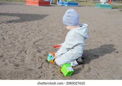 RUSSIA ABAKAN. May 1, 2021. Happy Little Child In A Gray Tracksuit And Adidas Hat Plays In The Sand.