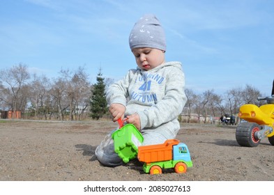 RUSSIA ABAKAN. May 1, 2021. Happy Little Child In A Gray Tracksuit And Adidas Hat Plays In The Sand.