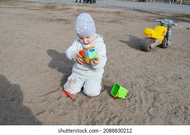 RUSSIA ABAKAN. May 1, 2021. Happy Little Child In A Gray Tracksuit And Adidas Hat Plays In The Sand.