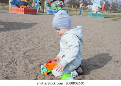 RUSSIA ABAKAN. May 1, 2021. Happy Little Child In A Gray Tracksuit And Adidas Hat Plays In The Sand.