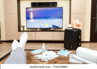 Russia, Abakan-April 2, 2020: A Person Is Watching TV. A Sick Person At Home In Quarantine Dreams Of Traveling And Looks At The Sea And The Beach On TV, Next To Medical Masks And Medicines