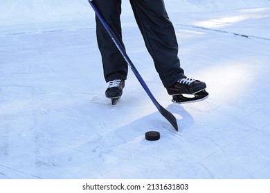 Russia, Chelyabinsk, February 14, 2022: Man on skates stands on an ice rink and holds a hockey stick in his hands, a puck lies on the ice. Only the legs are visible. Street hockey game.