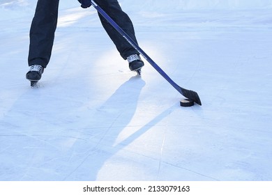 Russia, Chelyabinsk, February 14, 2022: Man on skates stands on an ice rink and holds a hockey stick in his hands, a puck lies on the ice. Only the legs are visible. Street hockey game.